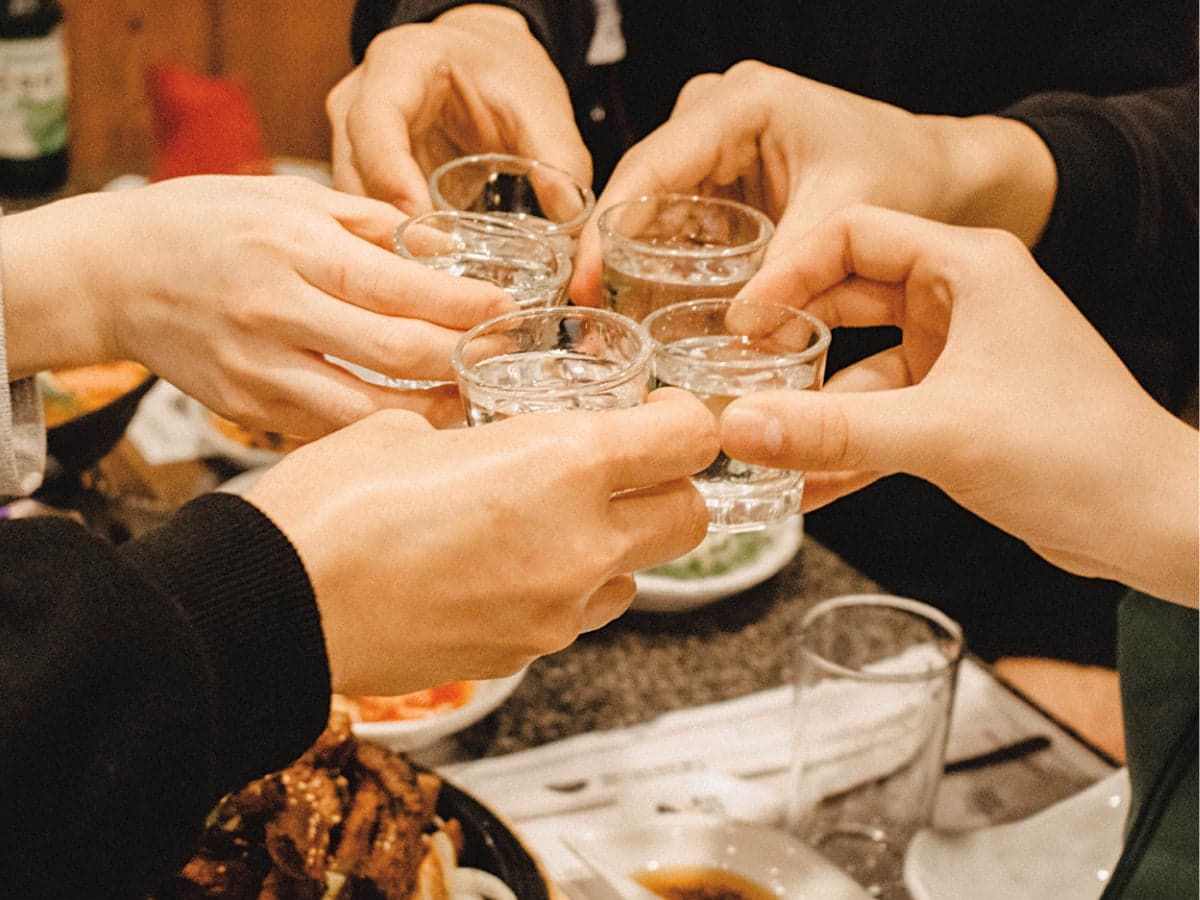 At a Korean restaurant, people are toasting with glasses full of soju.