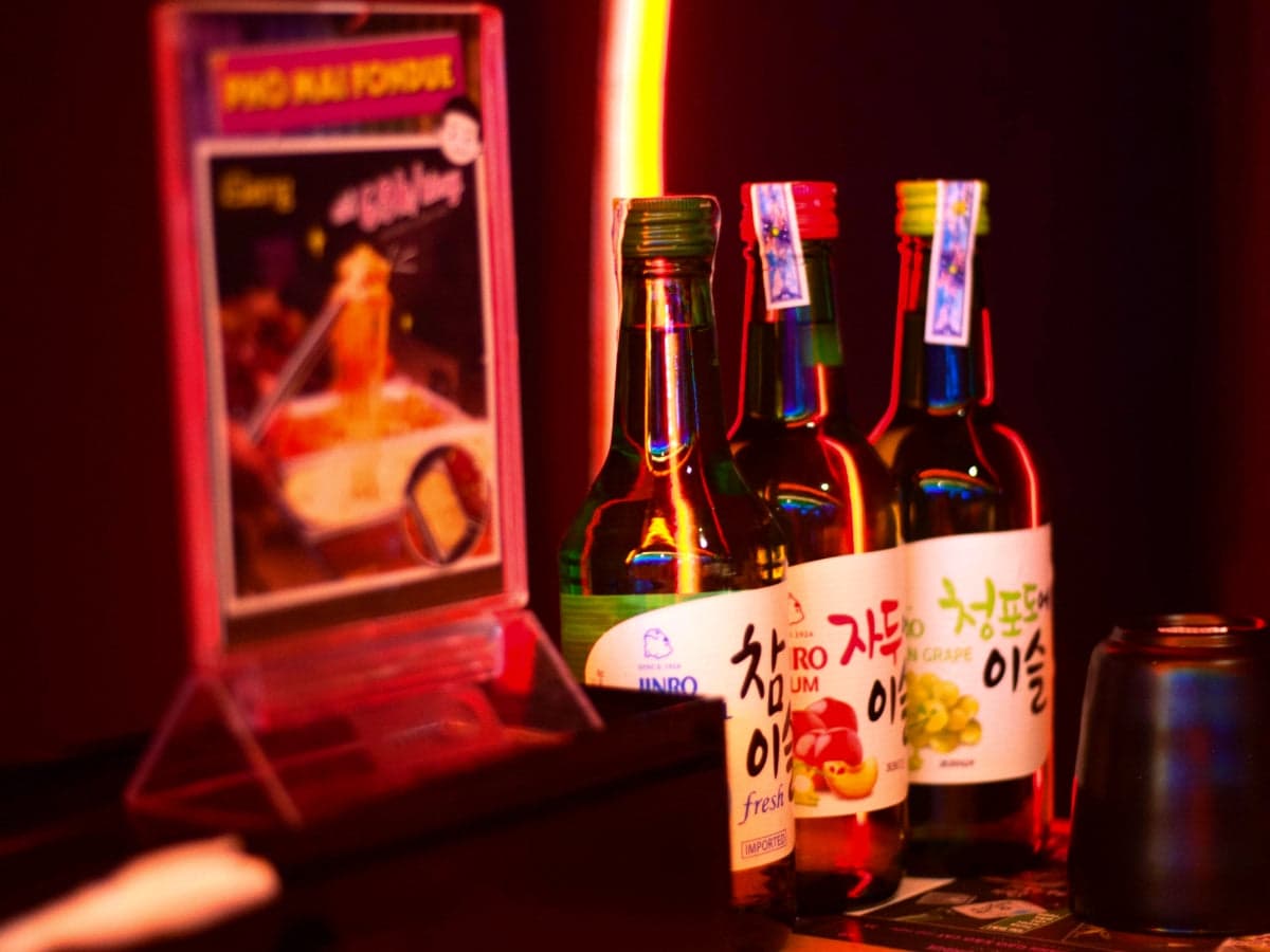 three different varieties of Chamisul Soju on the bar table, one bottle each in fresh, plum, and green grape